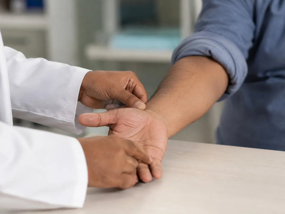 Doctor examining a patient's hand and forearm resting on a clinic table
