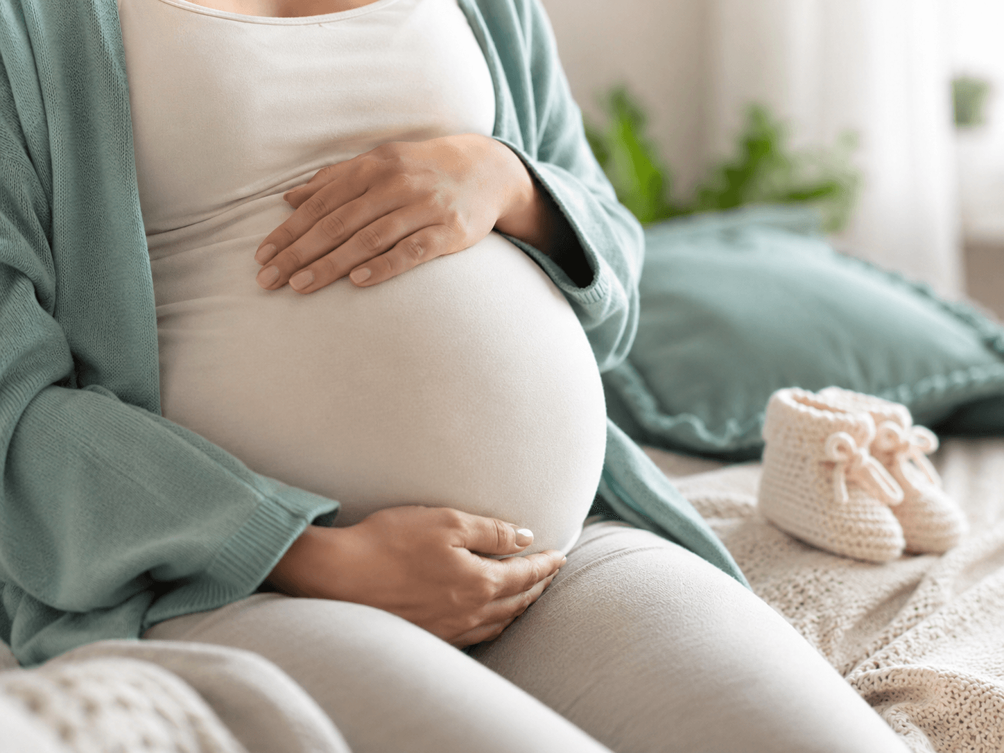 An expectant mother's hands cradling her pregnant belly in soft daylight