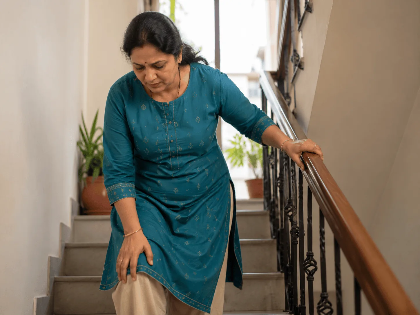Woman pausing on a staircase holding the rail with a hand on her knee